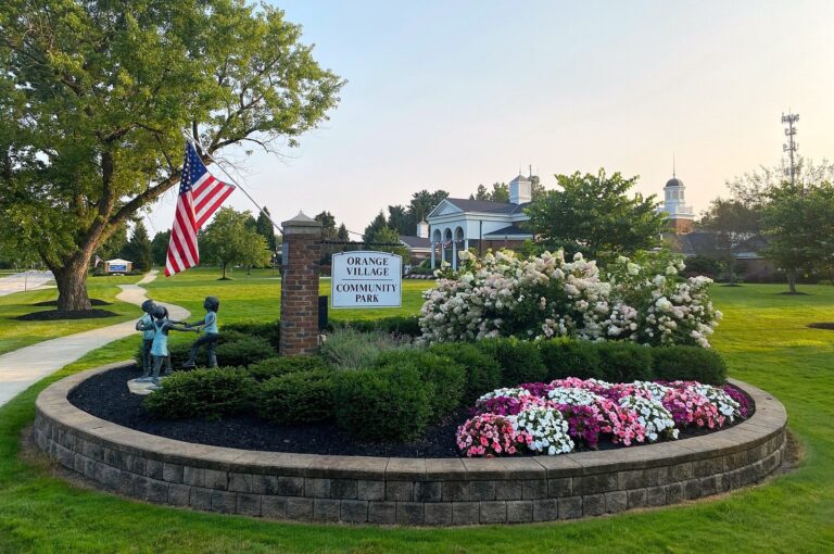 Orange Village Community Park entrance sign framed by flowering shrubs and a large tree